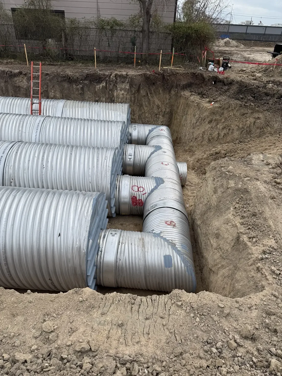 Close view of large corrugated metal pipe header and manifold connections inside an open-cut excavation