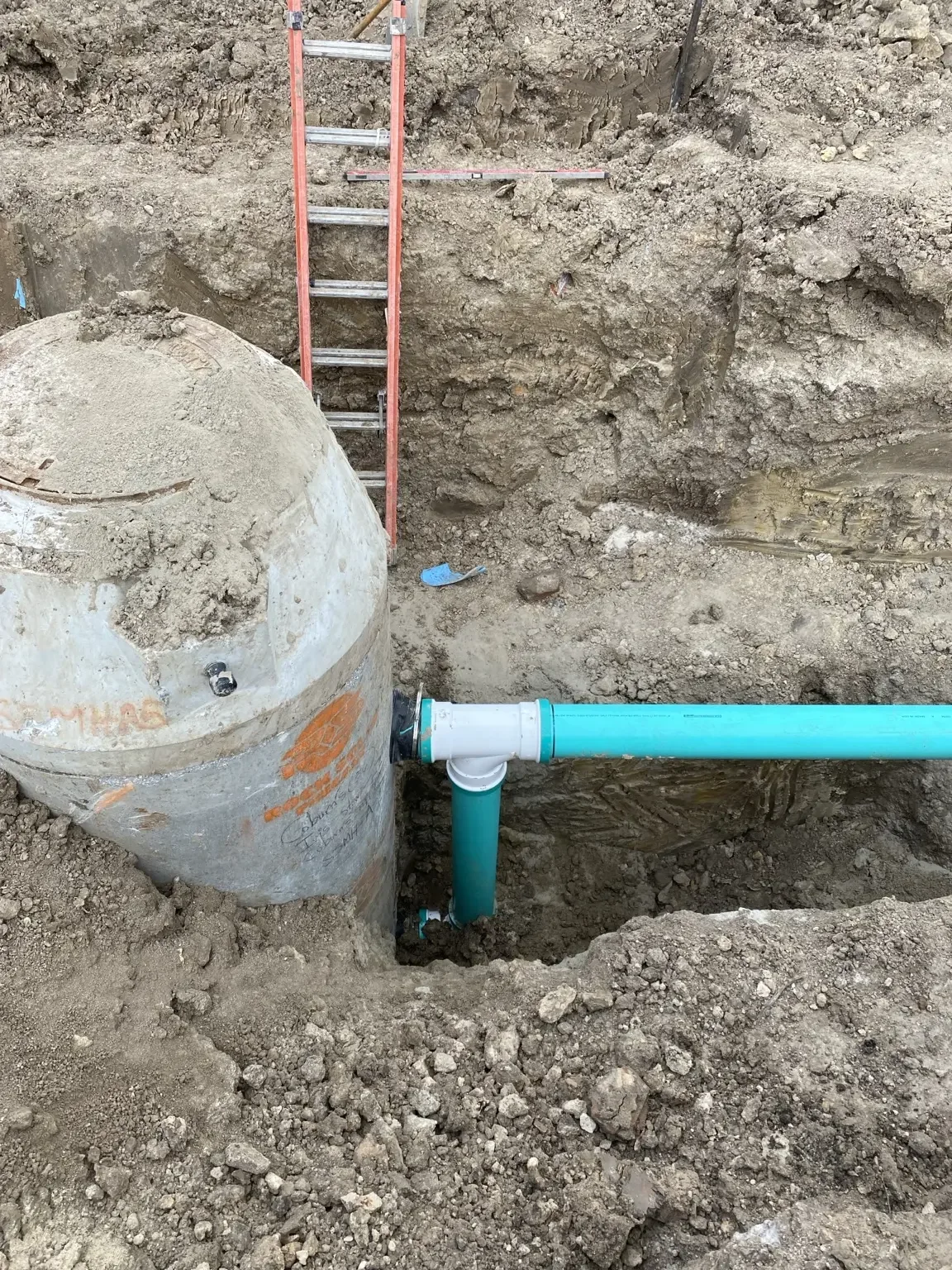 Precast concrete manhole structure in a dirt excavation with a green PVC sewer pipe connection