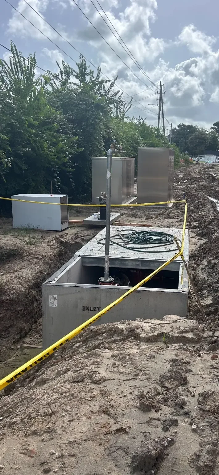 Precast concrete lift station structure marked INLET set in an excavation with stainless control cabinets behind it