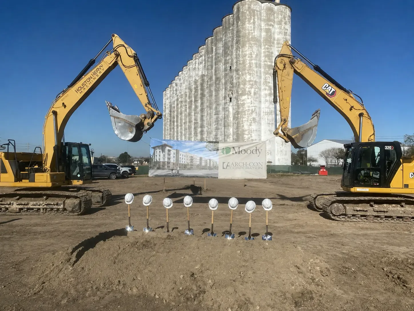 Two excavators framing a line of ceremonial shovels at an active construction site.