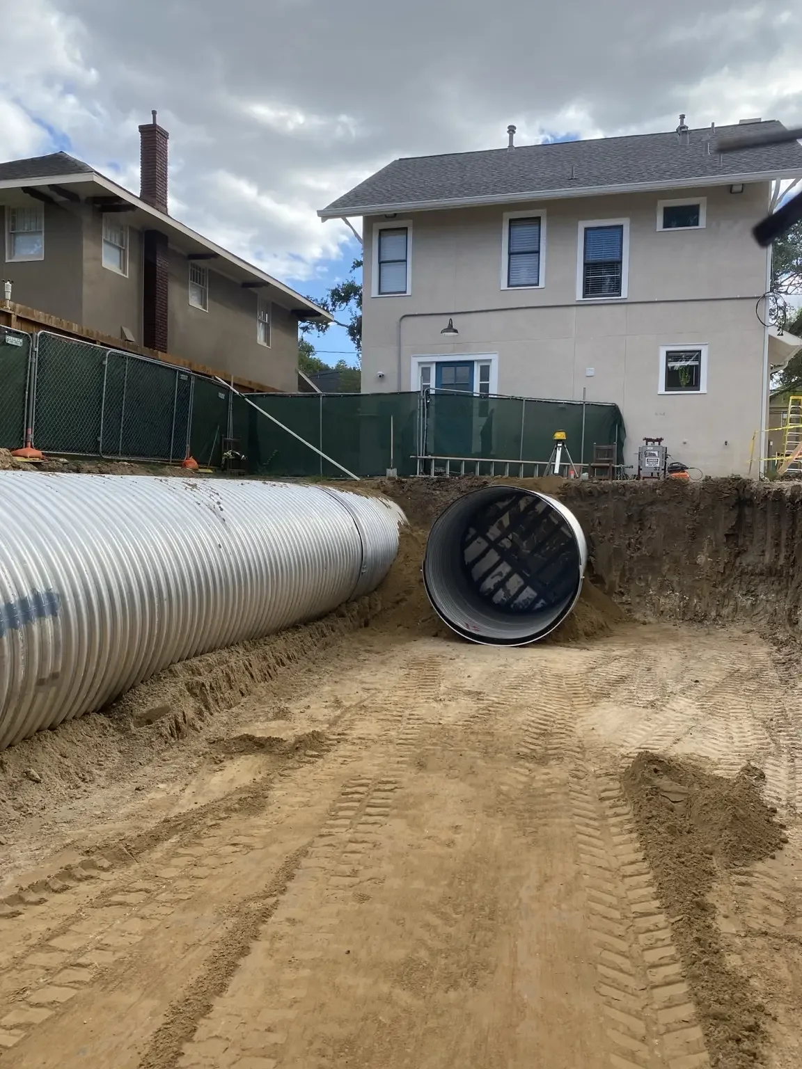 Large diameter corrugated metal pipe staged on the ground next to a deep excavation on a developed site
