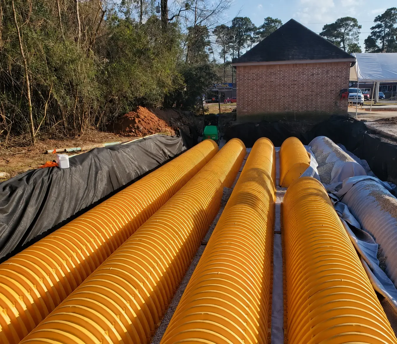 Rows of arched plastic stormwater detention chambers set on crushed stone bedding over black geotextile fabric