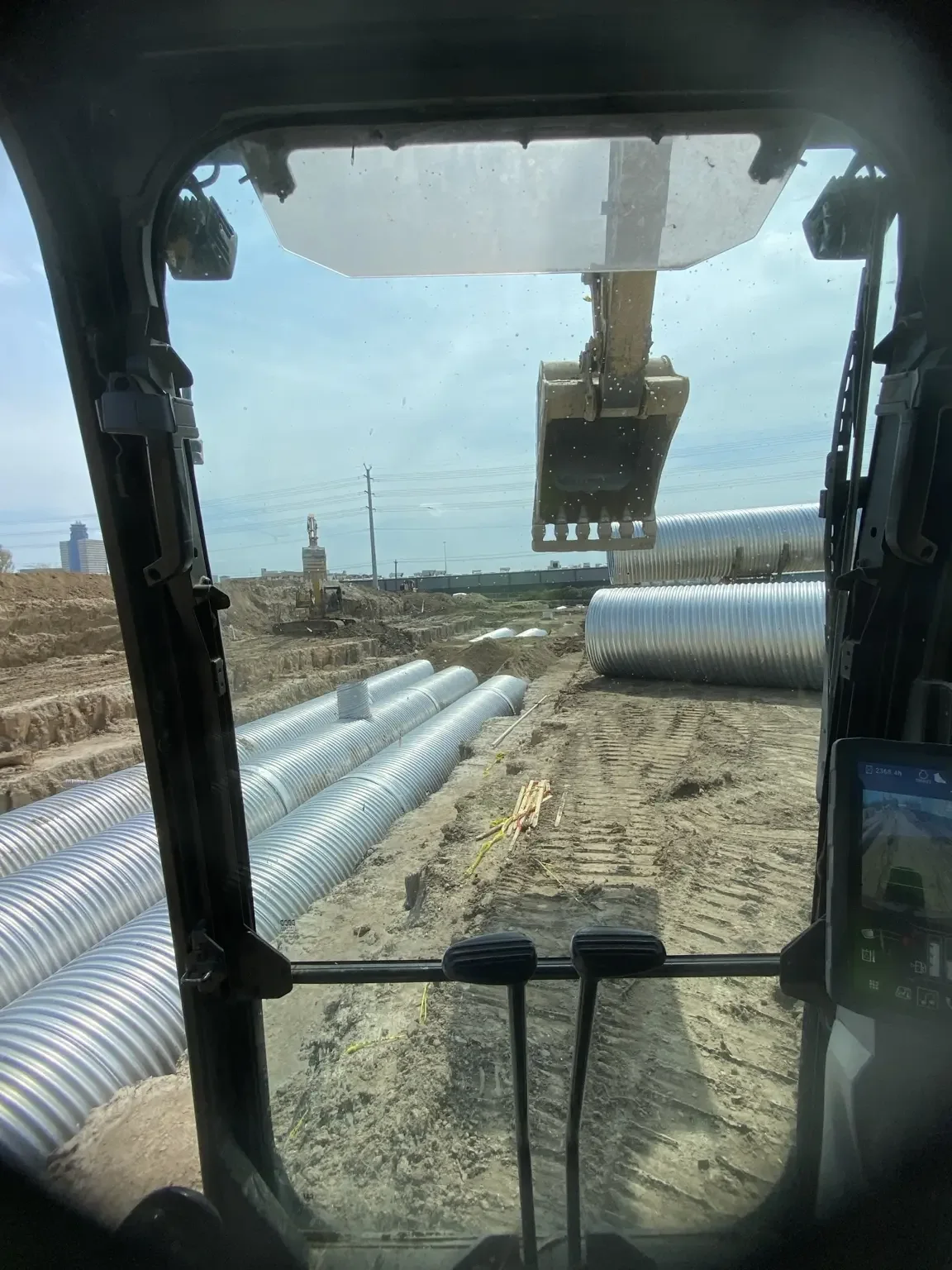 View from an excavator cab looking out over rows of corrugated metal detention pipe being placed in trenches