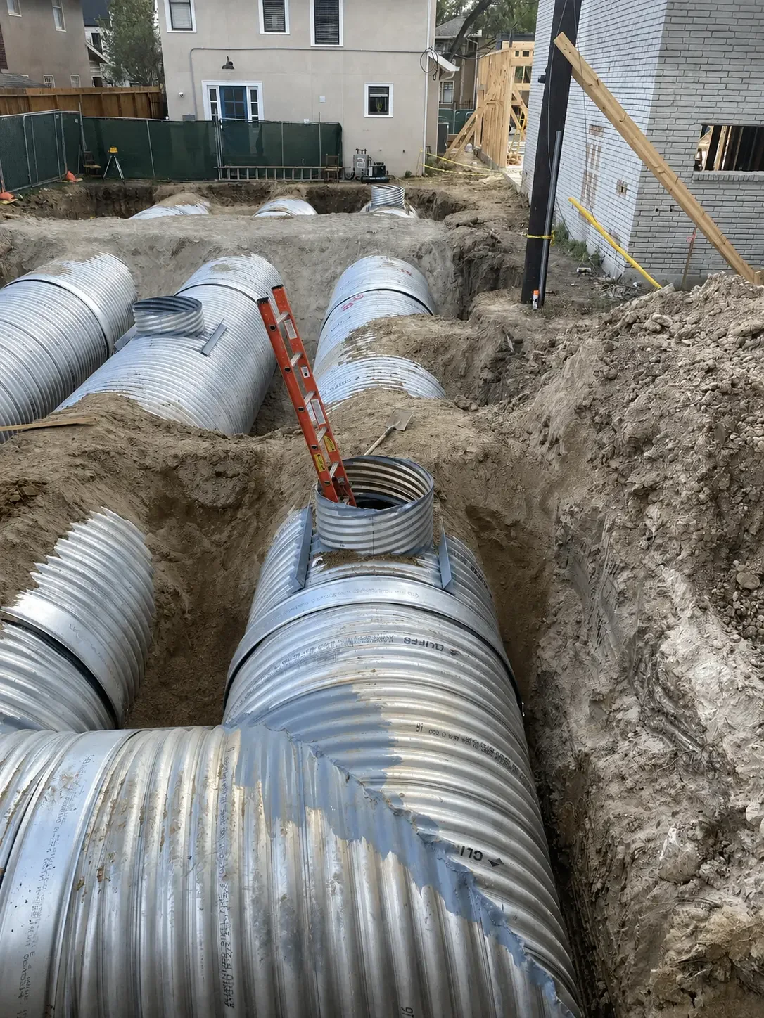 Large corrugated metal detention pipe being installed on a tight construction lot bordered by existing buildings