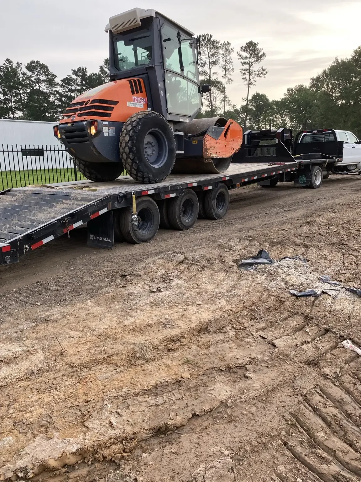 Padfoot soil compaction roller loaded on a gooseneck trailer at the edge of a graded site